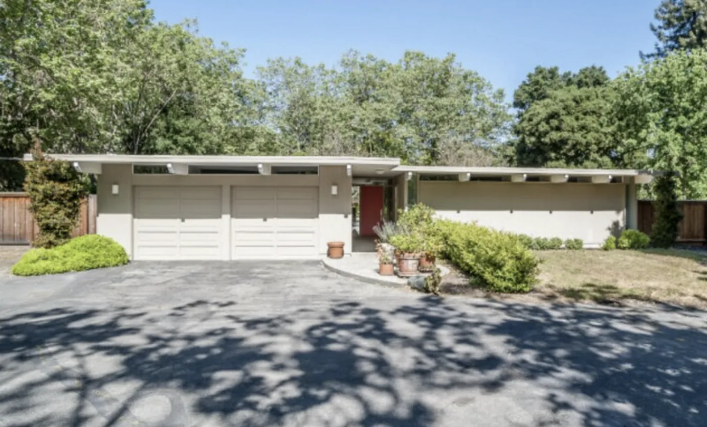 The street front of an Atherton Eichler: two pale garage doors and a red front door set back under a low-pitched roof, with a band of clerestory windows running above.
