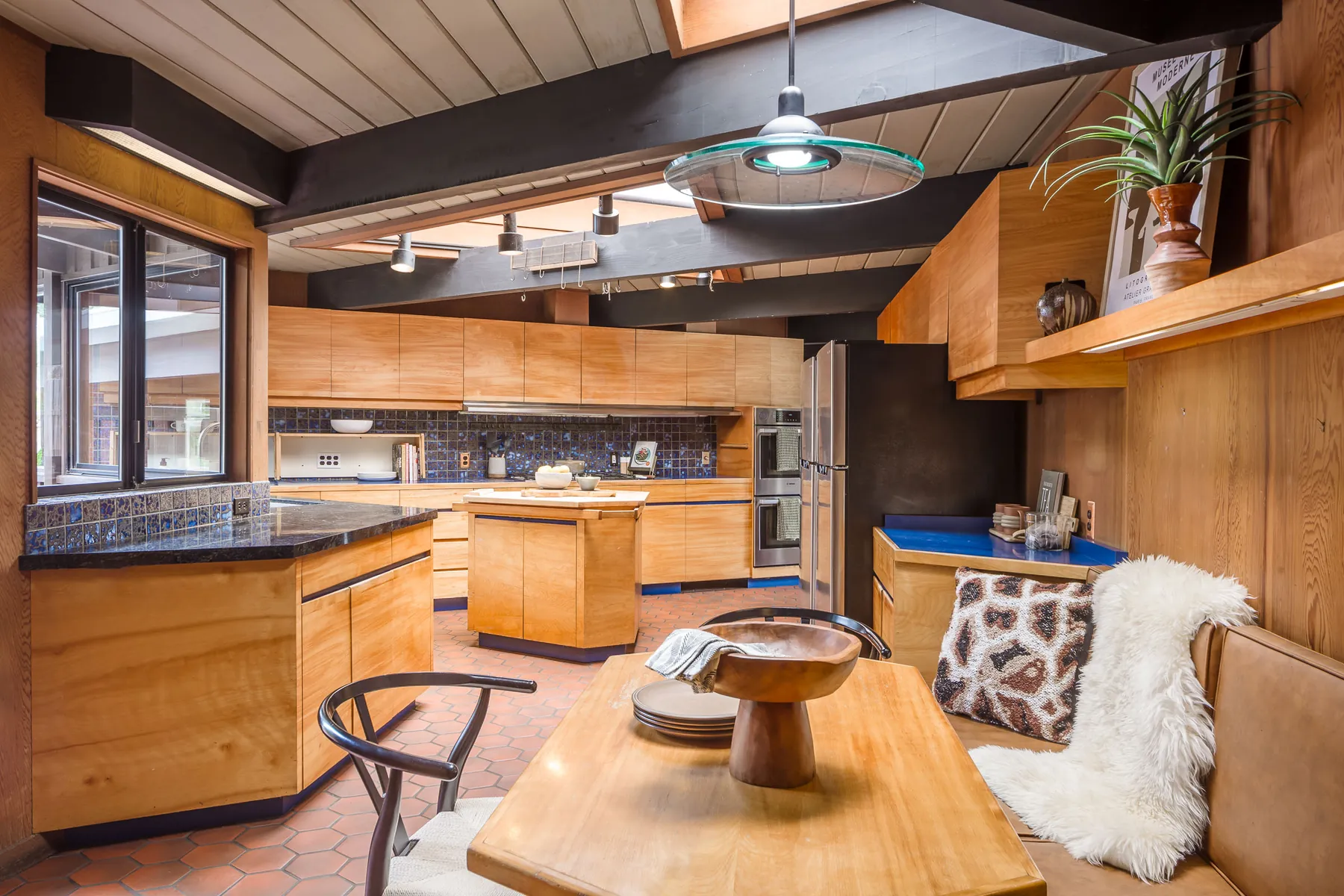 Kitchen with blond wood cabinetry, a blue tile backsplash, a hexagonal tile floor, dark exposed beams and skylights, and a built-in breakfast banquette.