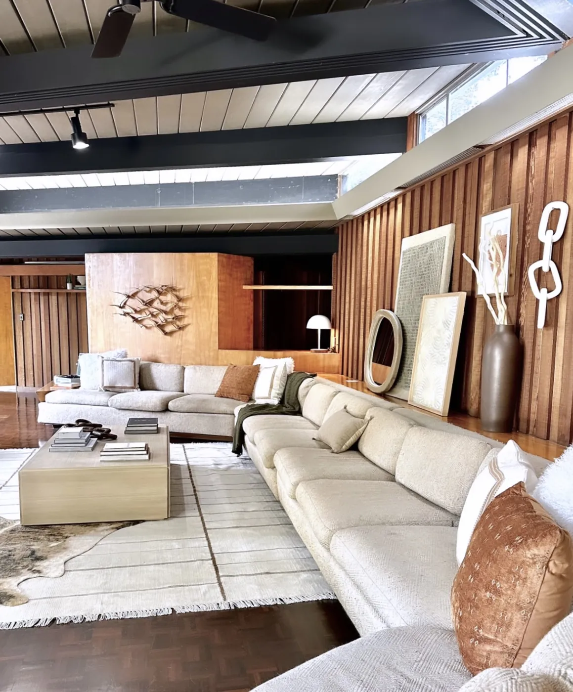 The living room: two long sofas on a parquet floor, dark exposed beams under a pale board ceiling, a clerestory window band above vertical redwood panelling, and a plywood partition beyond.
